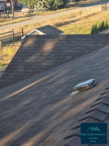 Aerial view of a newly installed asphalt shingle roof with a metal box vent, overlooking a gravel road, pasture fencing and a red house in the background; Wright's Roofing & Construction Inc watermark in the corner.