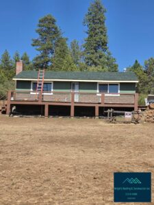 A single-story green cabin with a new dark green shingle roof, brick chimney and long brown wood deck, with an orange extension ladder leaning against the eaves and tall pine trees behind it under a clear blue sky; a Wright's Roofing & Construction inc logo appears in the lower right corner.