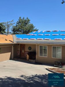 A single-story tan house mid-roof-replacement, with blue synthetic underlayment installed and stacked shingle bundles spread across the roof deck, exposed plywood over the garage, and an air compressor and hose on the driveway; watermarked Wright's Roofing & Construction Inc.